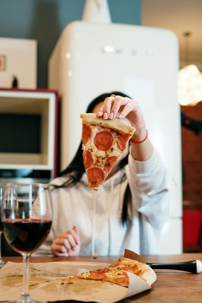 pexels-photo-4004465-4004465 Woman enjoying a slice of pepperoni pizza and a glass of red wine at home.