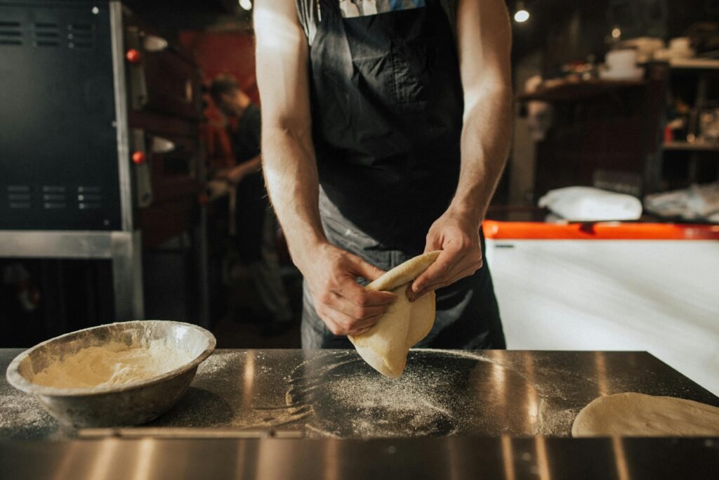 pexels-photo-5056624-5056624 Close-up of a chef preparing pizza dough in a pizzeria kitchen.
