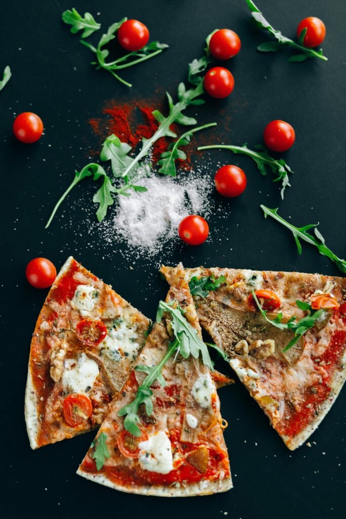 pexels-photo-5792329-5792329 Top view of gourmet pizza slices with arugula, cherry tomatoes, and spices on a dark surface.